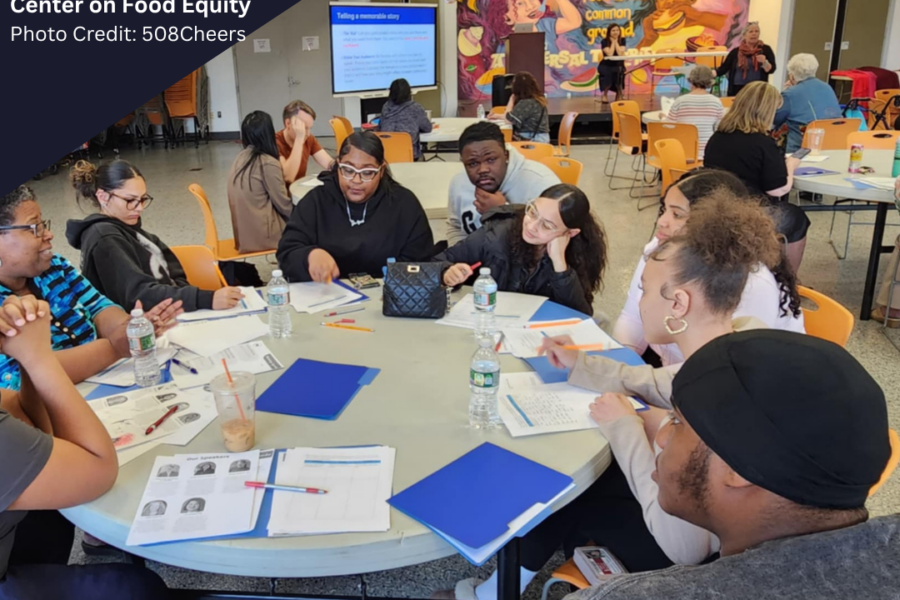 A photo from a Center on Food Equity event, showing speakers at the front of a gymnasium, and several tables of people engaged in conversation.